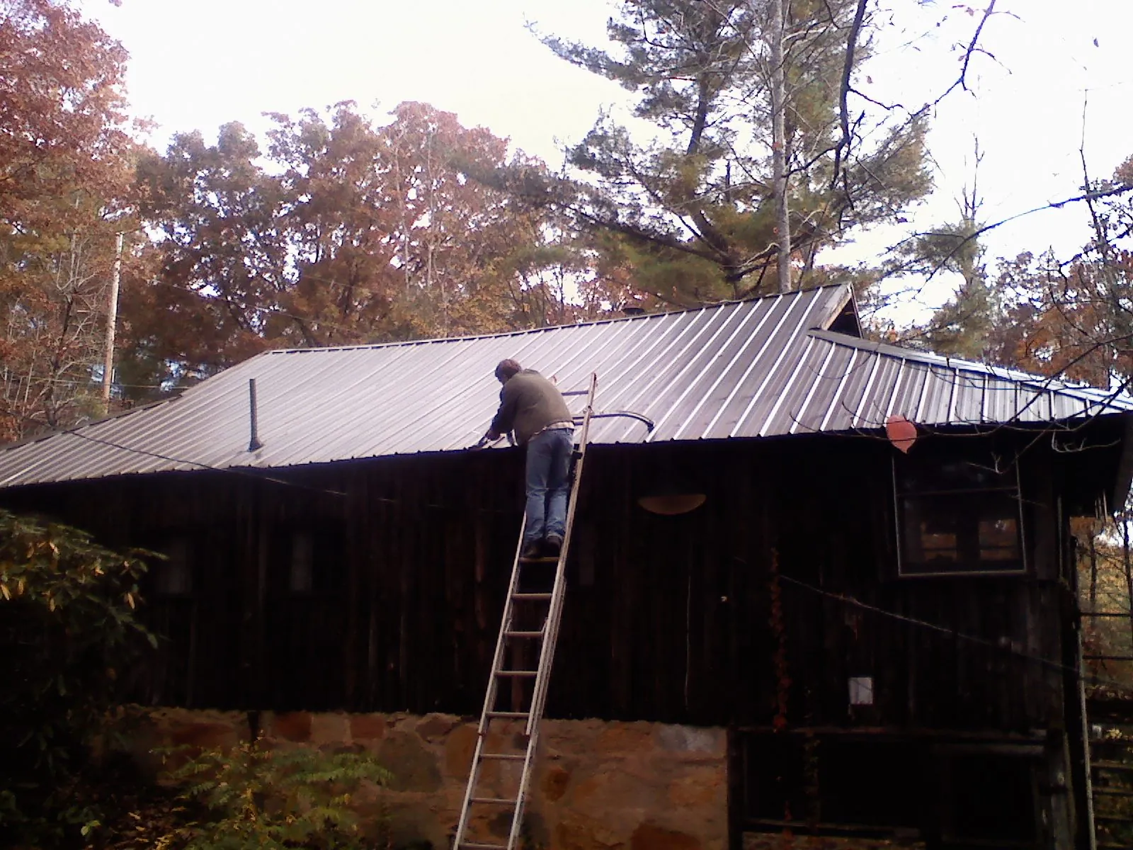 Roofer on a ladder working along the edge of a cabin metal roof in Brookfield